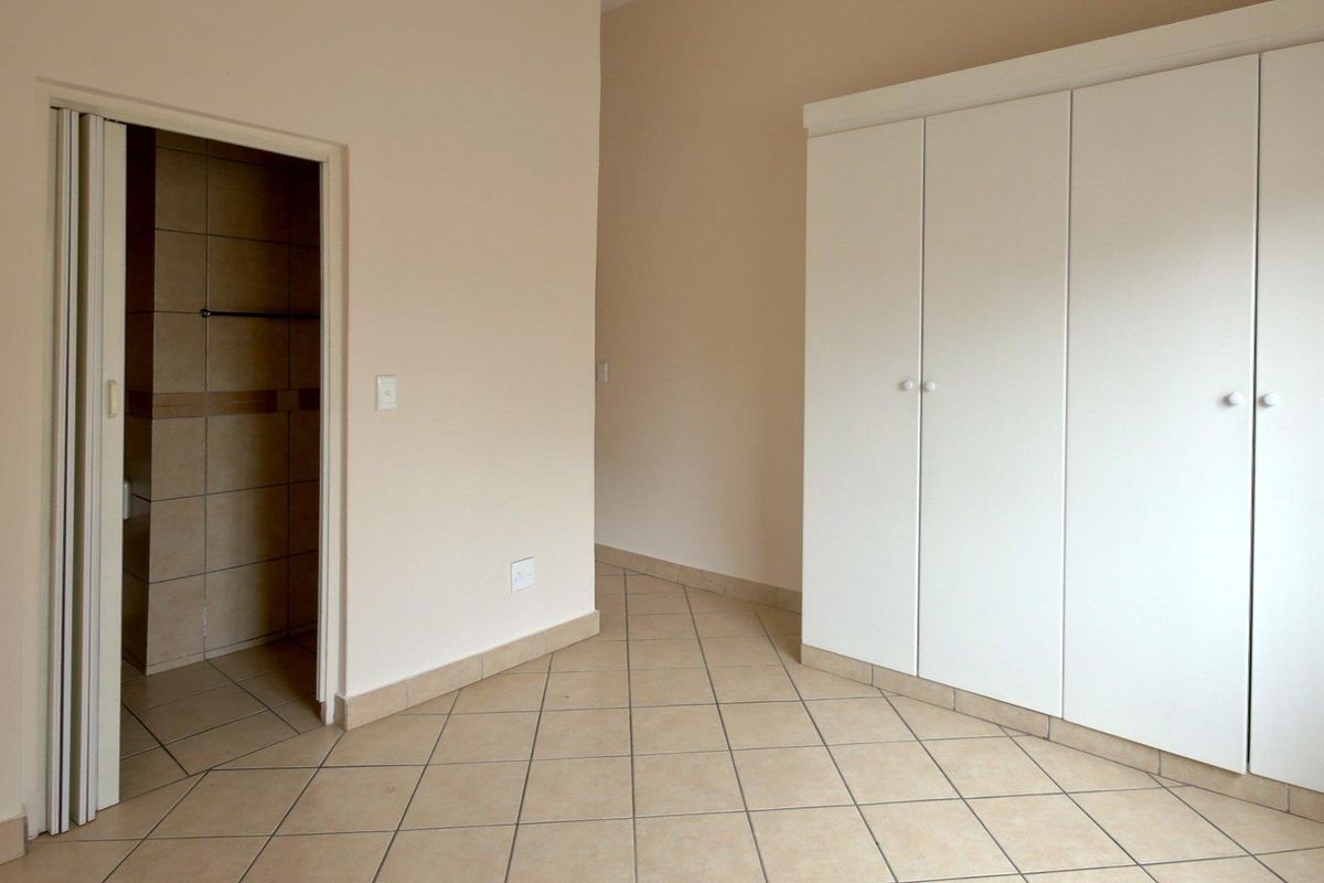 An empty bedroom featuring neutral tiled flooring, built-in white cupboards, and a folding door leading to an en-suite bathroom.