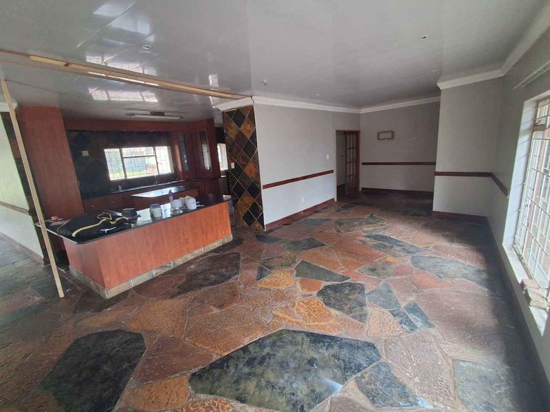 Spacious open-plan living and kitchen area featuring unique stone tile flooring, built-in cabinetry, and a central kitchen island, ready for renovation.
