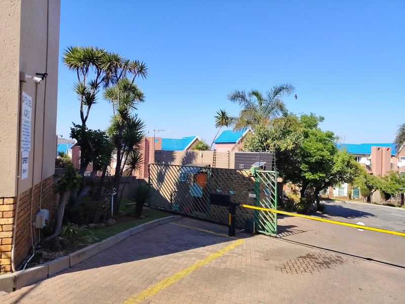 View of the townhouse complex entrance featuring a security gate, electric fencing, and paved driveway access.