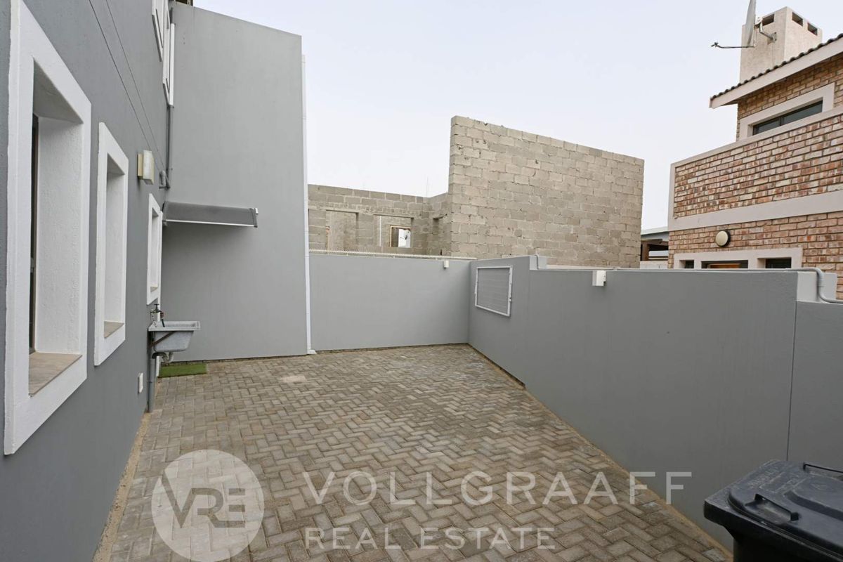 A paved rear courtyard area featuring a utility sink and boundary walls, with an adjacent unfinished masonry structure visible.