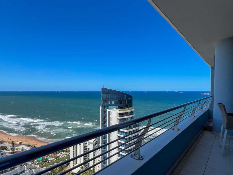 A spacious balcony featuring a modern stainless steel balustrade and tiled flooring, offering expansive panoramic ocean and coastal views.