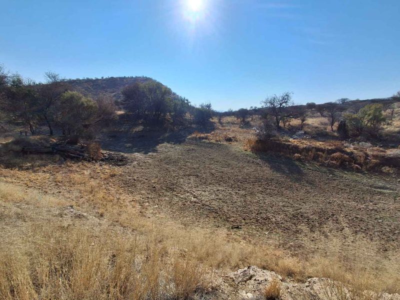 A wide-angle view of the natural landscape on the small holding, featuring dry terrain, indigenous vegetation, and surrounding hills under a clear sky.