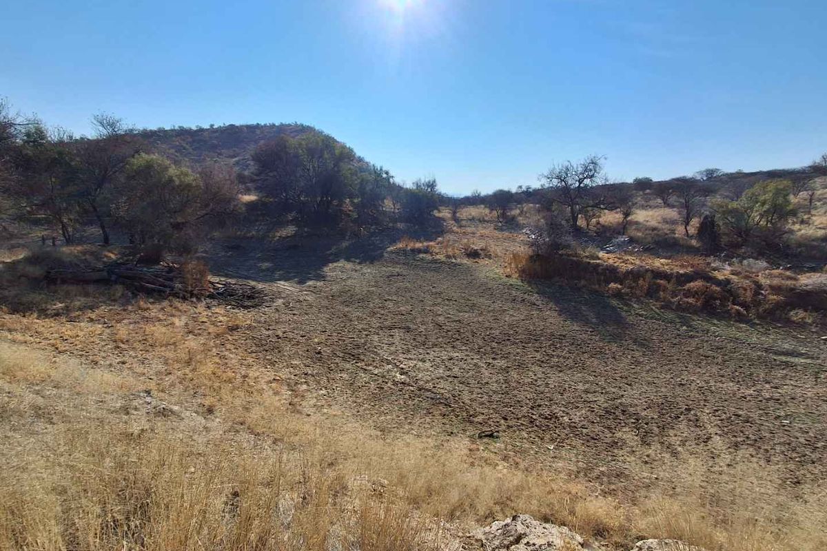 A wide-angle view of the natural landscape on the small holding, featuring dry terrain, indigenous vegetation, and surrounding hills under a clear sky.