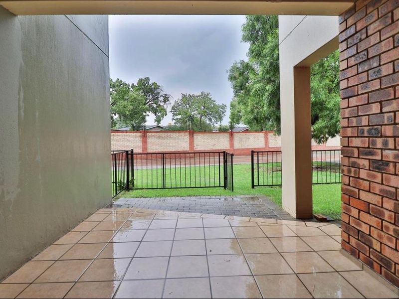 A covered patio area featuring tiled flooring, brick accents, and direct access to a small fenced garden space.