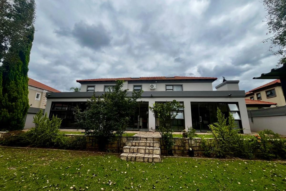 Rear view of a modern two-story house featuring large glass sliding doors, a stone-clad staircase, and a well-maintained garden.