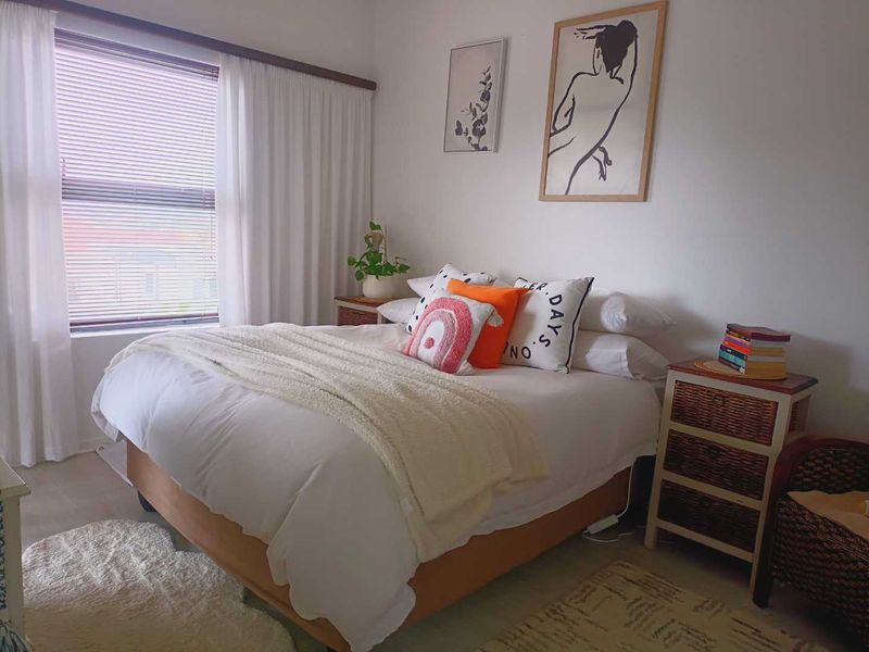 A well-lit bedroom featuring a large window with venetian blinds and neutral wall finishes.