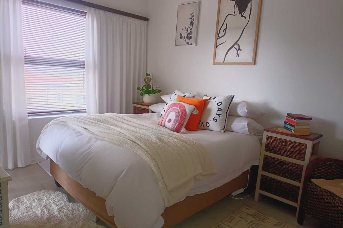 A well-lit bedroom featuring a large window with venetian blinds and neutral wall finishes.