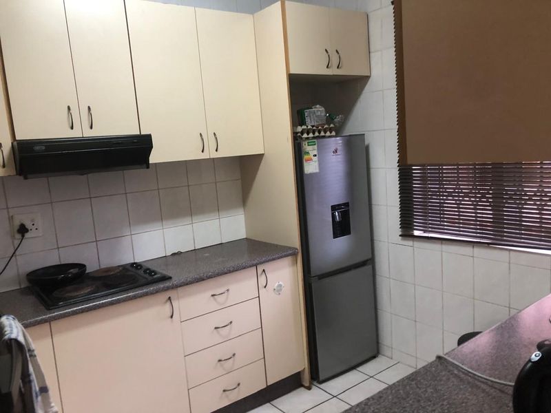 A functional kitchen featuring built-in cabinetry, laminate countertops, an electric hob with extractor fan, and tiled finishes throughout.