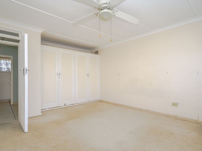 An empty bedroom featuring built-in cupboards, a ceiling fan, and neutral finishes, offering a blank canvas for renovation or restyling.