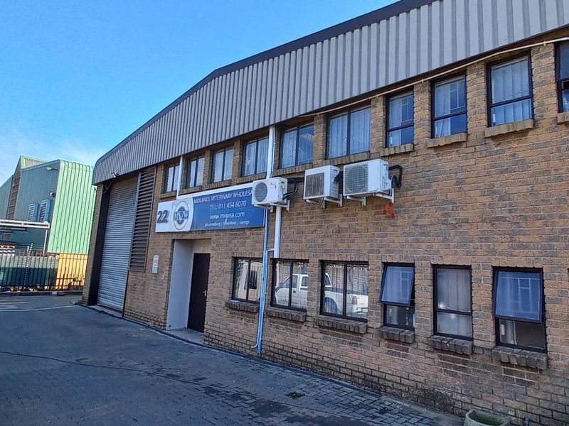 Exterior view of an industrial warehouse building featuring face-brick facade, metal roofing, roller shutter door, and multiple wall-mounted air conditioning units.