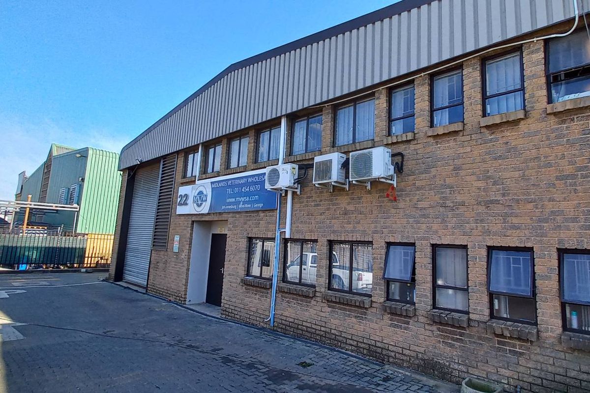 Exterior view of an industrial warehouse building featuring face-brick facade, metal roofing, roller shutter door, and multiple wall-mounted air conditioning units.