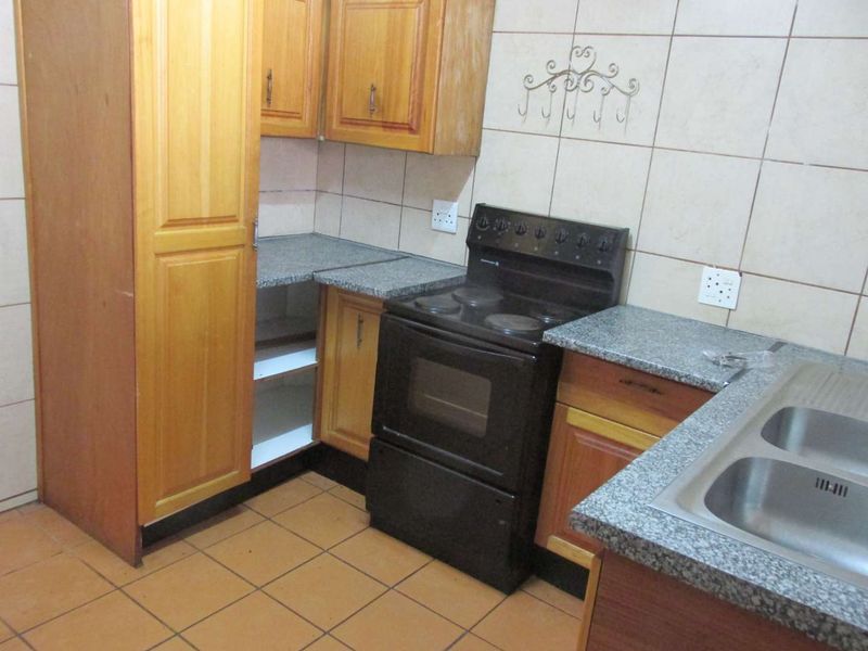 A functional kitchen featuring wooden cabinetry, granite countertops, a double bowl stainless steel sink, and a freestanding electric stove with tiled finishes.