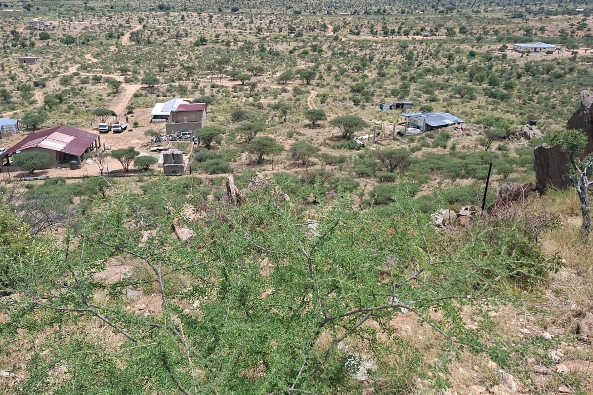 An elevated aerial view of a rural small holding property featuring multiple outbuildings with corrugated metal roofs set within a natural landscape.