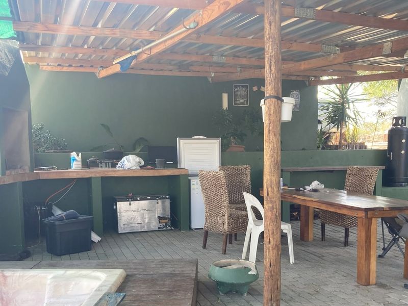 Covered outdoor patio area featuring a built-in braai, paved flooring, and timber structural supports, ideal for outdoor entertaining.