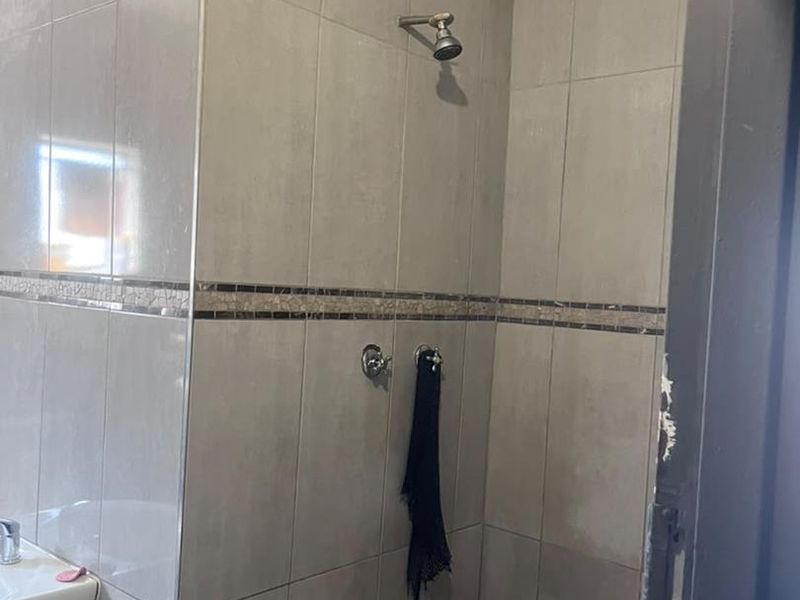 A functional bathroom shower area featuring neutral wall tiles with a decorative border and a pedestal basin.