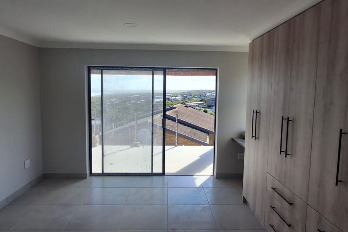 A bright, empty bedroom featuring modern built-in cupboards, tiled flooring, and a large sliding glass door that opens to a scenic outdoor view.