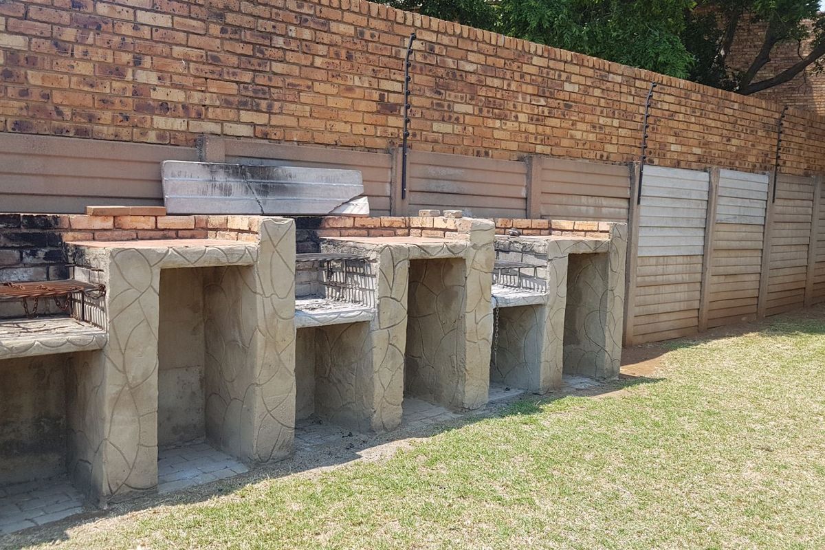 Outdoor area featuring a large, multi-section built-in brick braai facility set against a boundary wall with electric fencing.