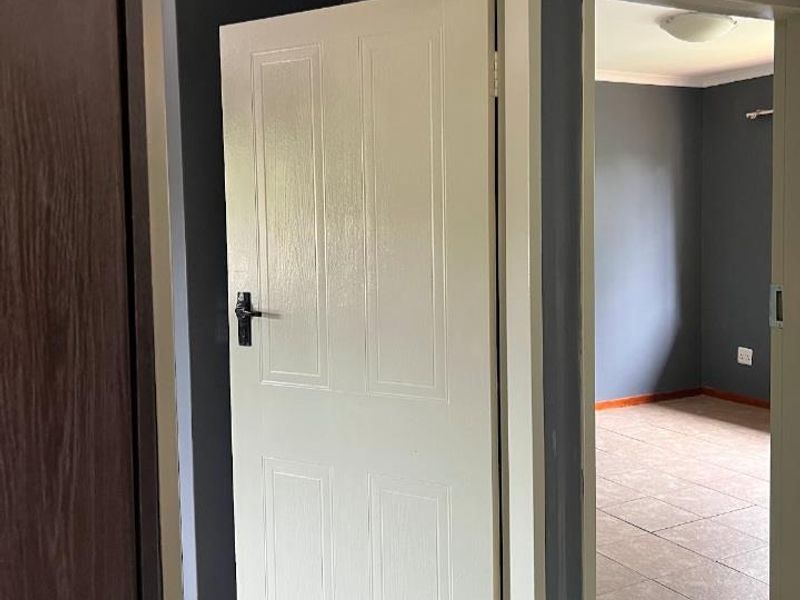 A view through a hallway into an adjacent empty room, featuring tiled flooring and neutral grey wall paint.