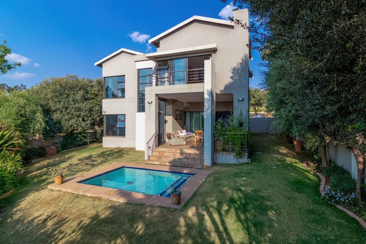Rear view of a two-story residential property featuring a swimming pool, landscaped garden, and a covered patio area with balcony access.