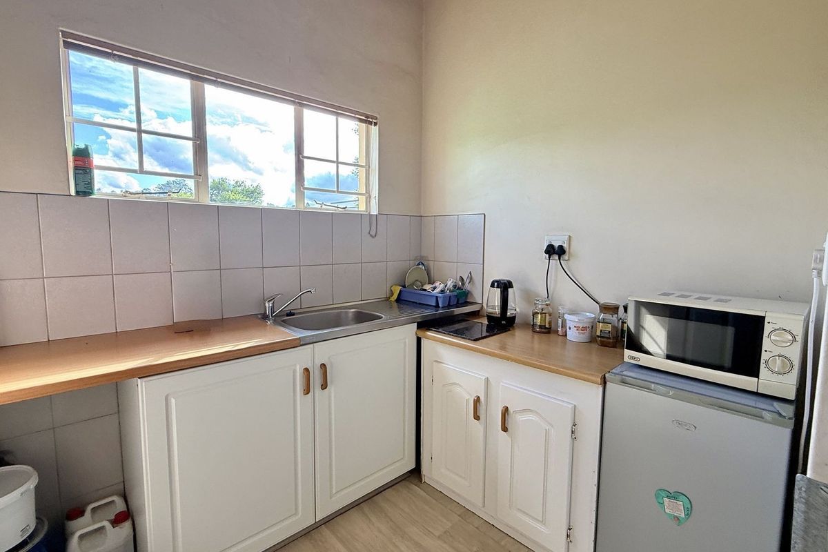 A functional kitchenette featuring white cabinetry, a stainless steel sink, tiled splashback, and wood-look laminate countertops.