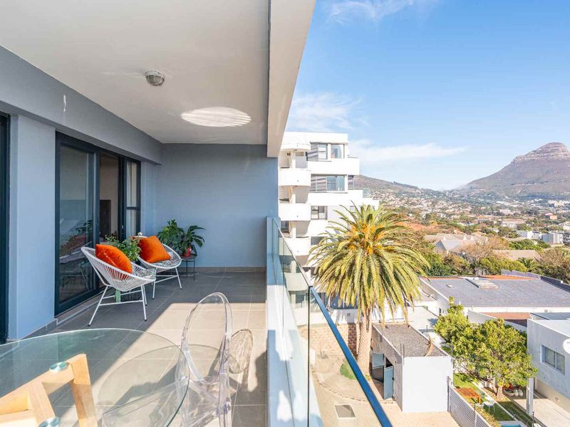 Spacious covered balcony featuring a modern glass balustrade and tiled flooring, offering expansive elevated views of the surrounding neighborhood and mountain landscape.