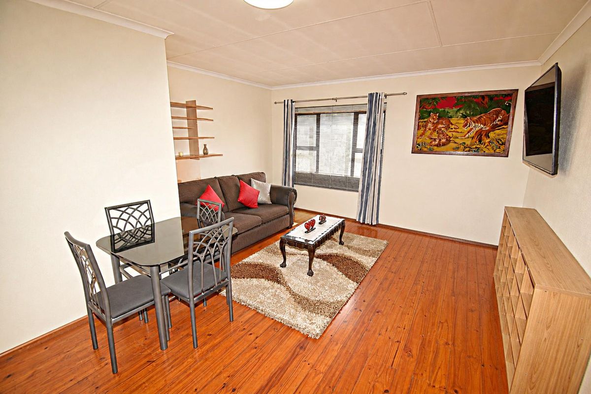 A well-maintained living room featuring warm-toned laminated wood flooring, neutral walls, and large windows with fitted blinds, offering a comfortable and functional living space.
