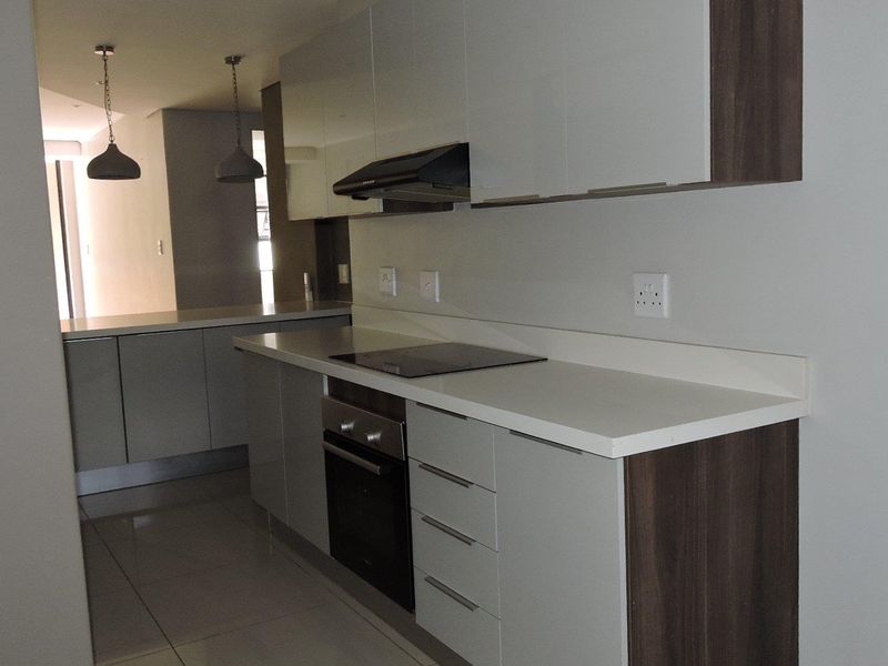 Modern kitchen featuring sleek built-in cabinetry, stone countertops, integrated electric hob, oven, and extractor fan, complemented by tiled flooring and contemporary pendant lighting.