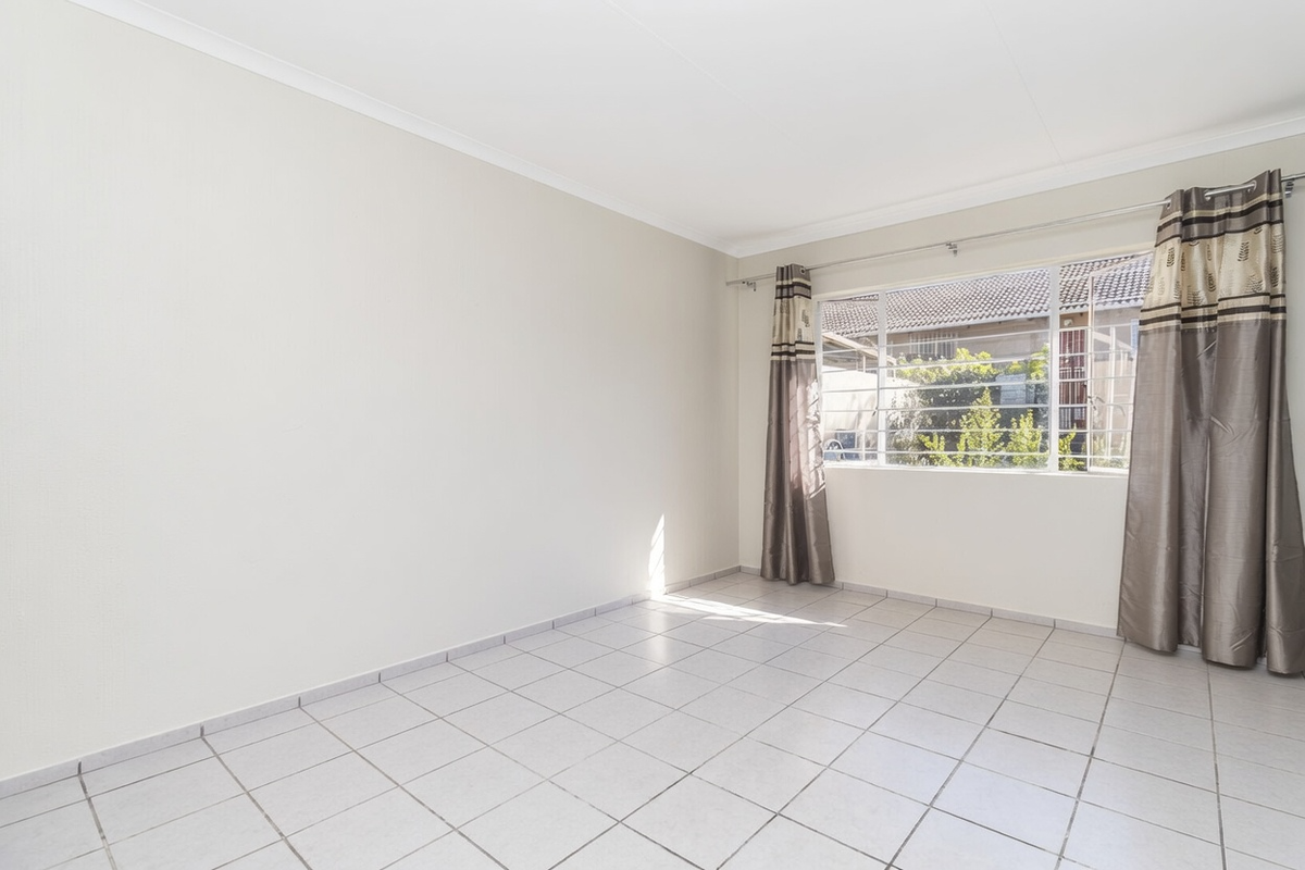A bright, empty bedroom featuring neutral tiled flooring, white walls, and a large window with security bars.