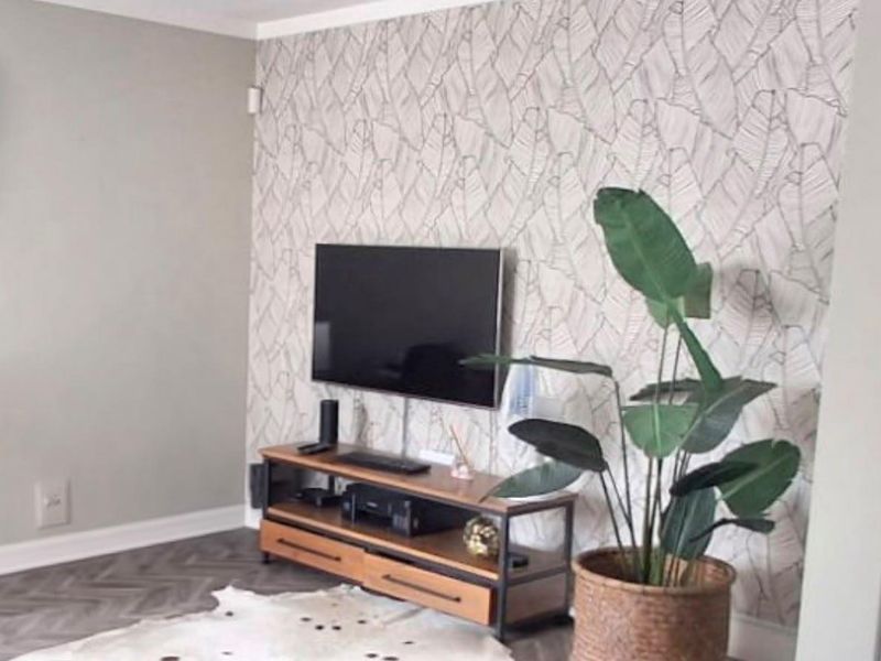A cozy living room area featuring stylish herringbone flooring and a decorative leaf-patterned feature wall.