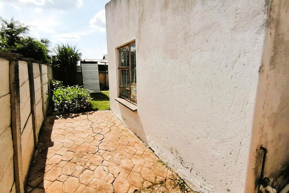 A view of the side exterior area featuring paved ground, a plain wall with a window, and a boundary wall.