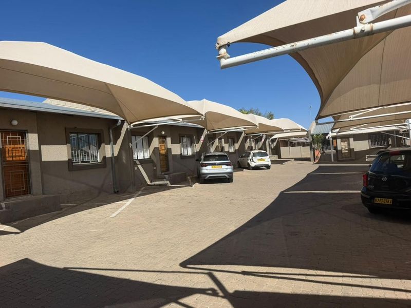 Exterior view of a townhouse complex featuring paved parking areas covered by shade sail structures and secure unit entrances.