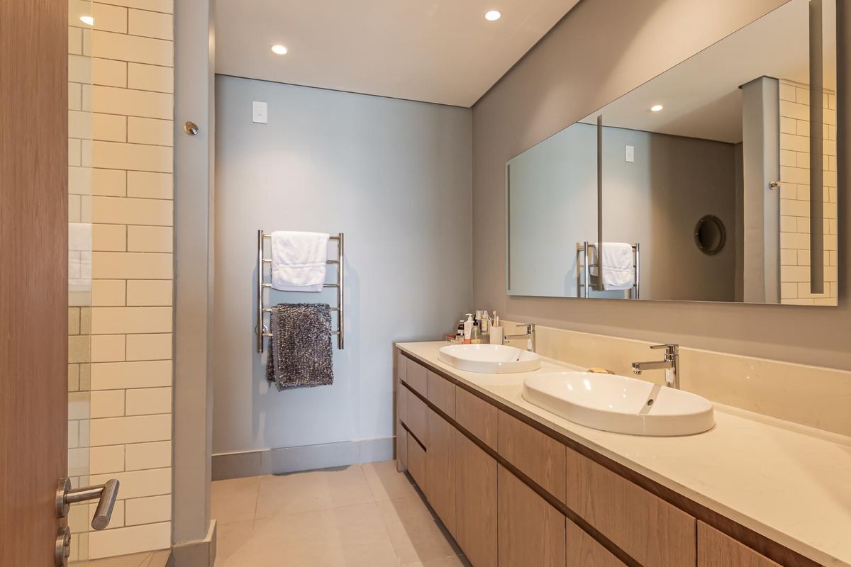 Modern bathroom featuring a double vanity with integrated sinks, stone countertop, large wall-mounted mirror, and a heated towel rail.