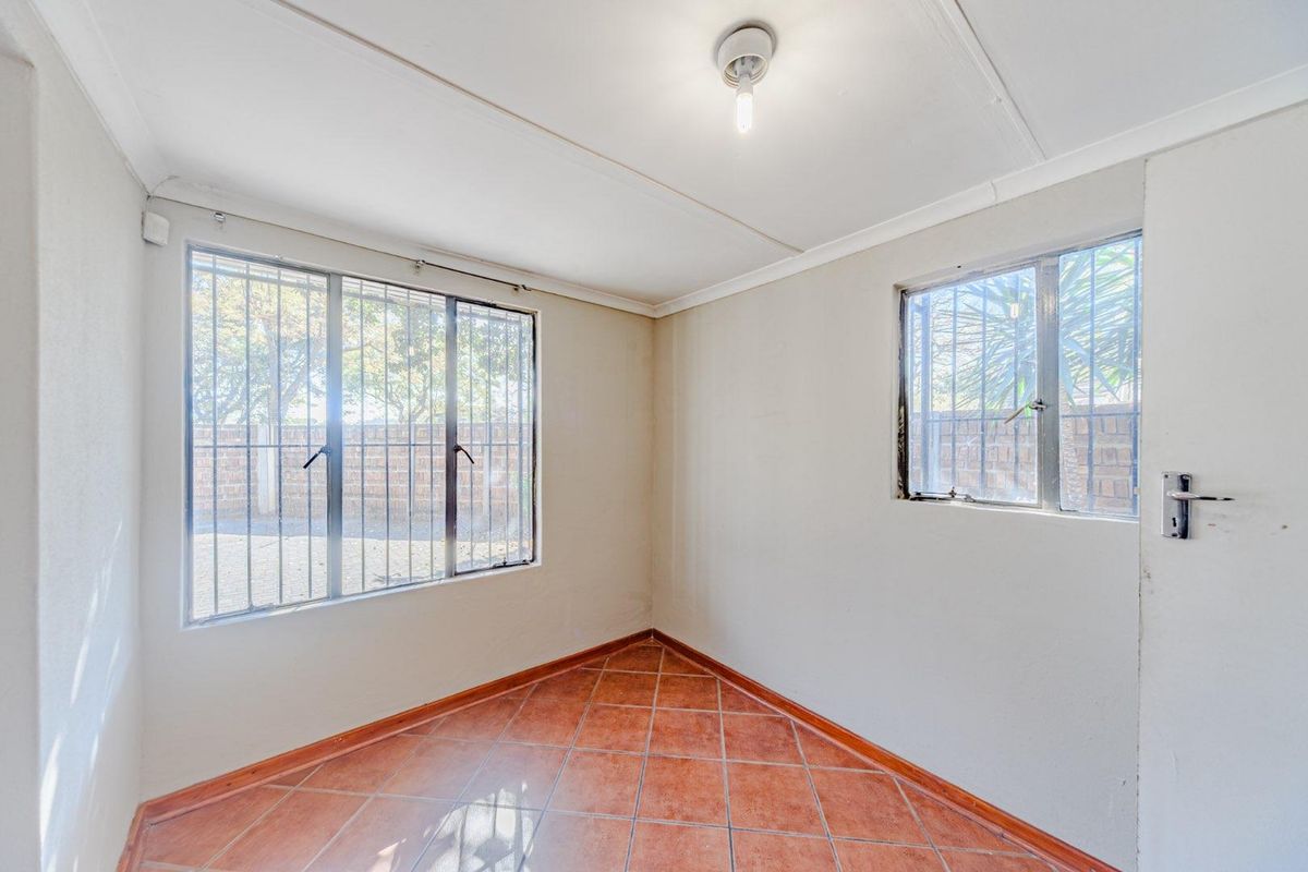 A vacant bedroom featuring tiled flooring, security bars on the windows, and neutral wall finishes, offering a blank canvas for personalization.