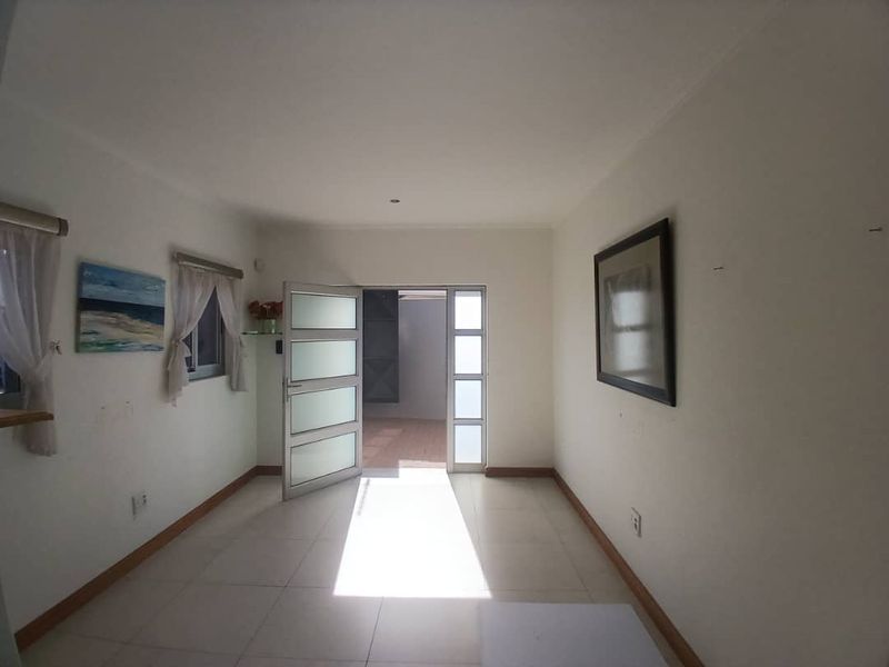 A bright, empty living area featuring tiled flooring and glass-panelled doors leading to an outdoor space.