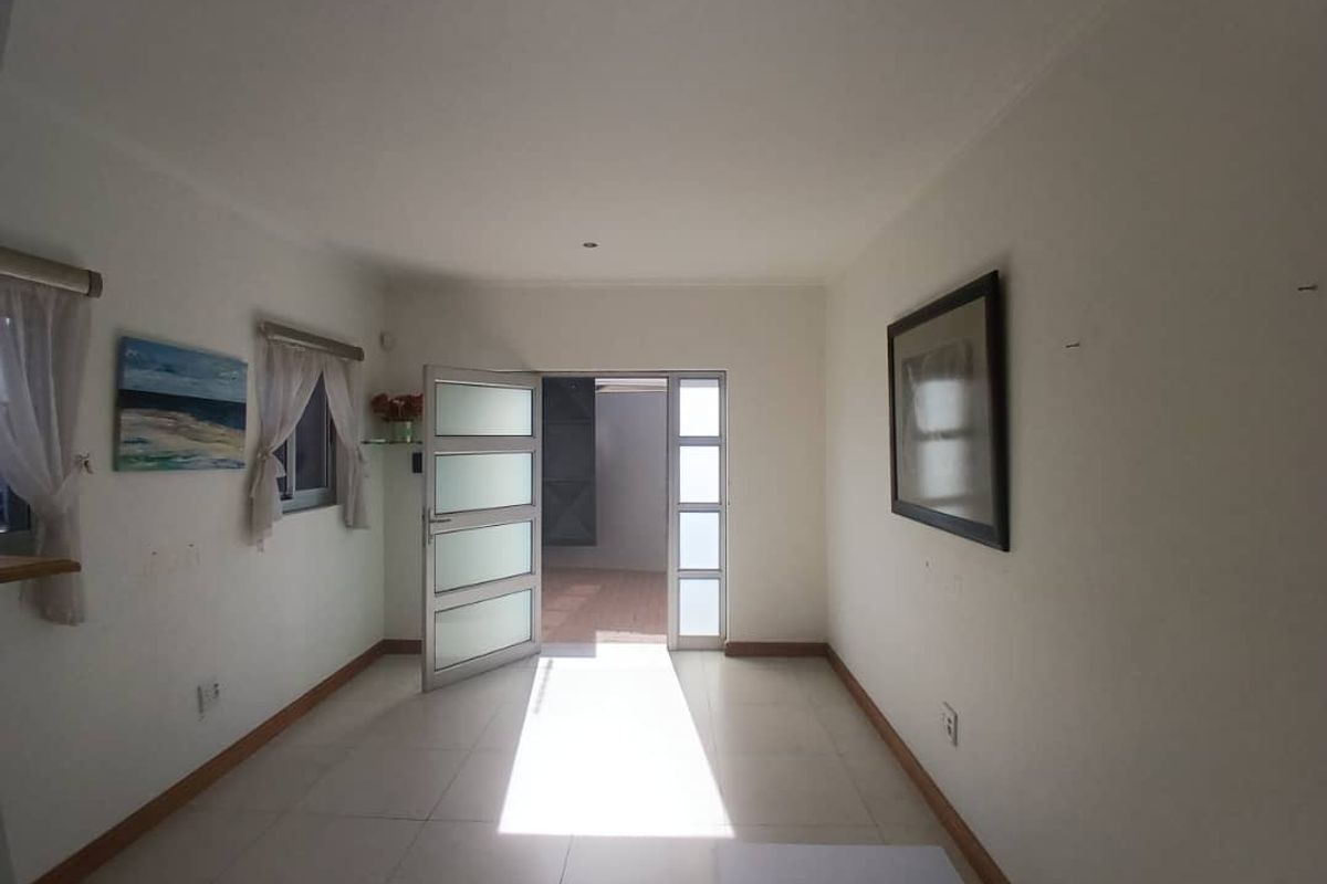 A bright, empty living area featuring tiled flooring and glass-panelled doors leading to an outdoor space.