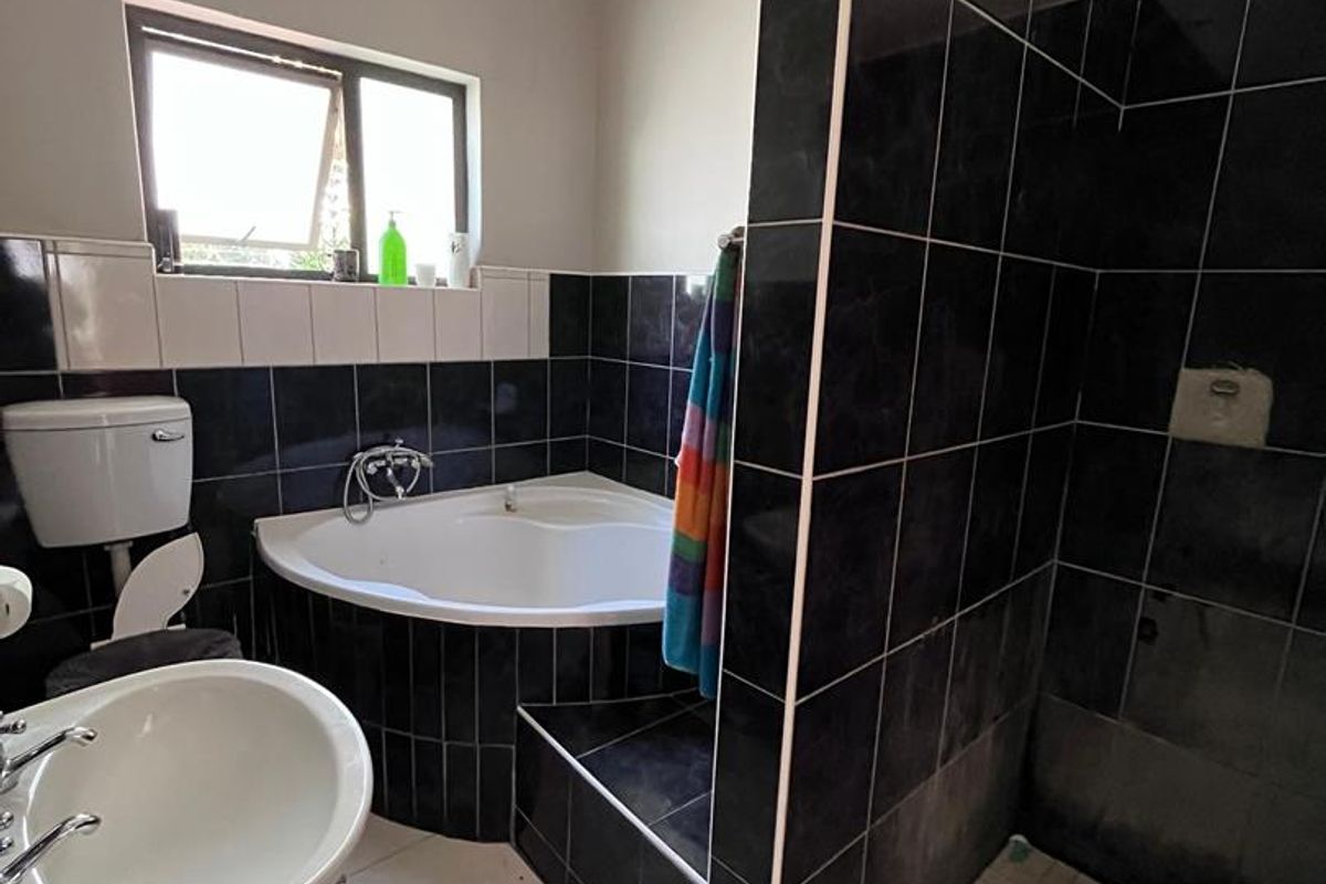 Bathroom featuring a corner bathtub, a separate walk-in shower with dark wall tiling, and a pedestal basin.