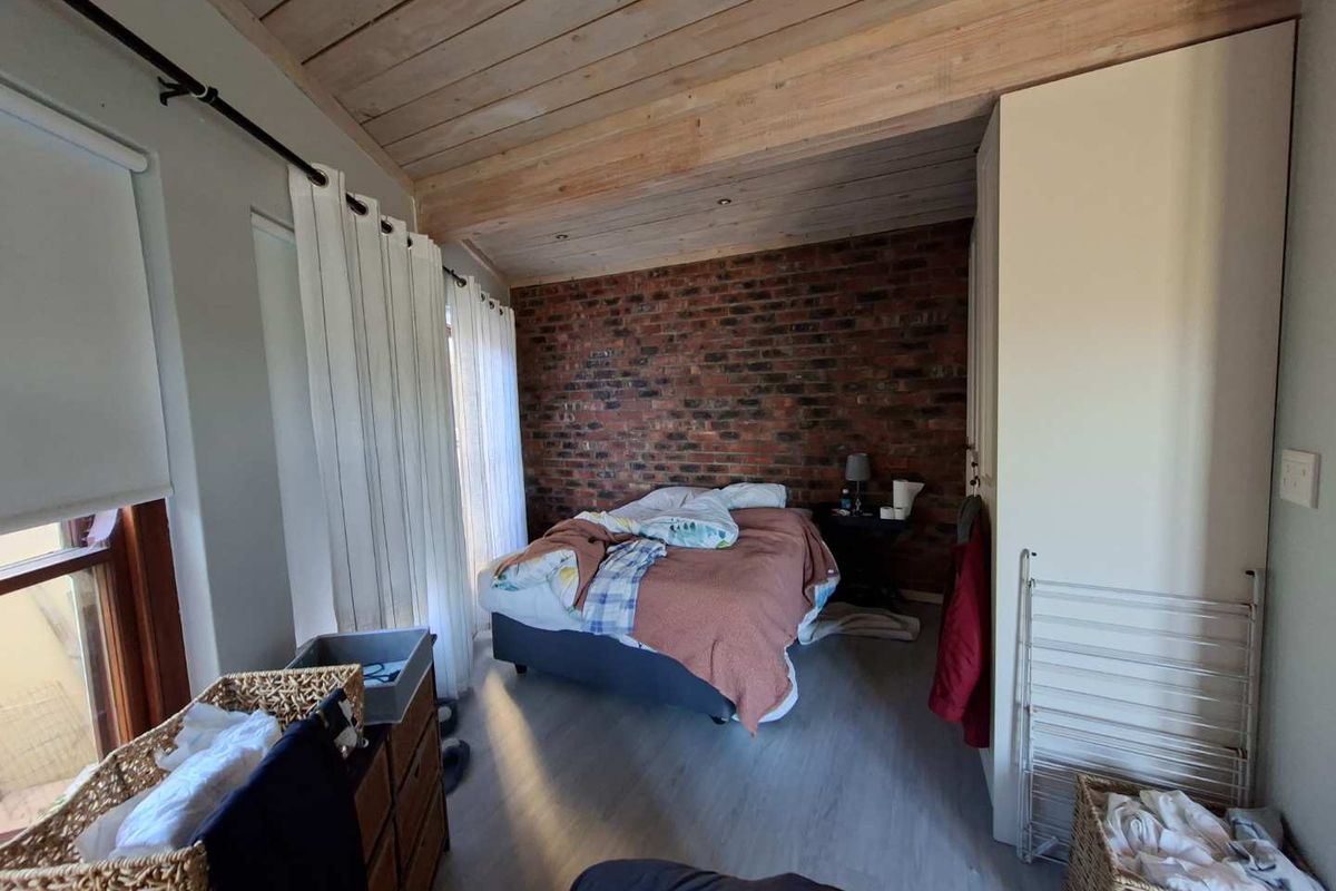 A bedroom featuring an exposed brick feature wall, timber ceiling, and built-in wardrobe storage.
