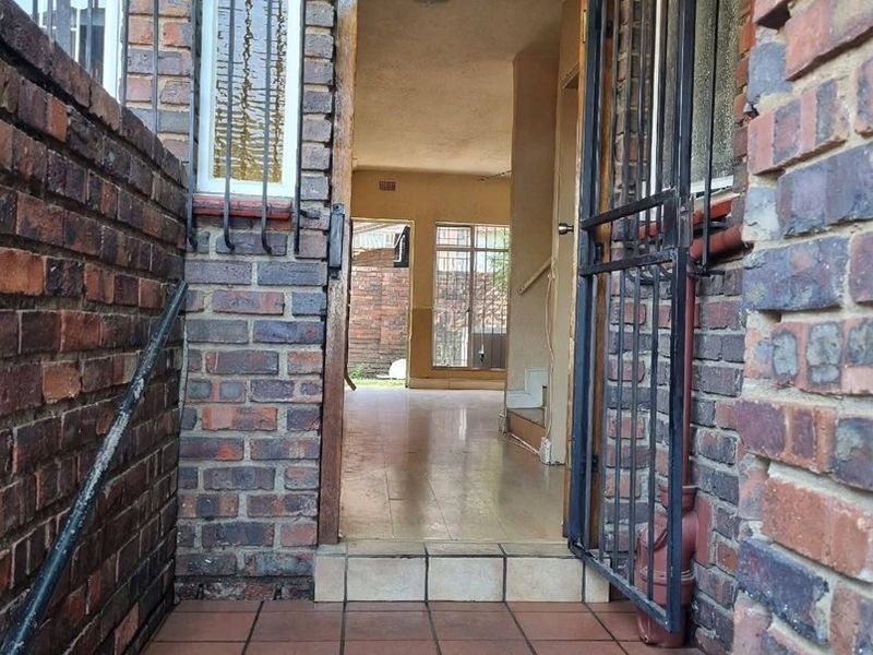 Entrance area featuring face brick exterior, security gate, and tiled steps leading into an open-plan interior space.