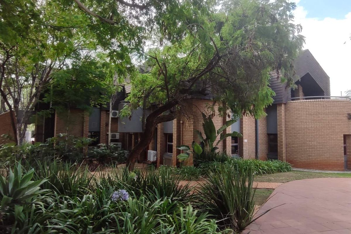 Exterior view of a face brick office building featuring a paved walkway, mature landscaping, and integrated security infrastructure.