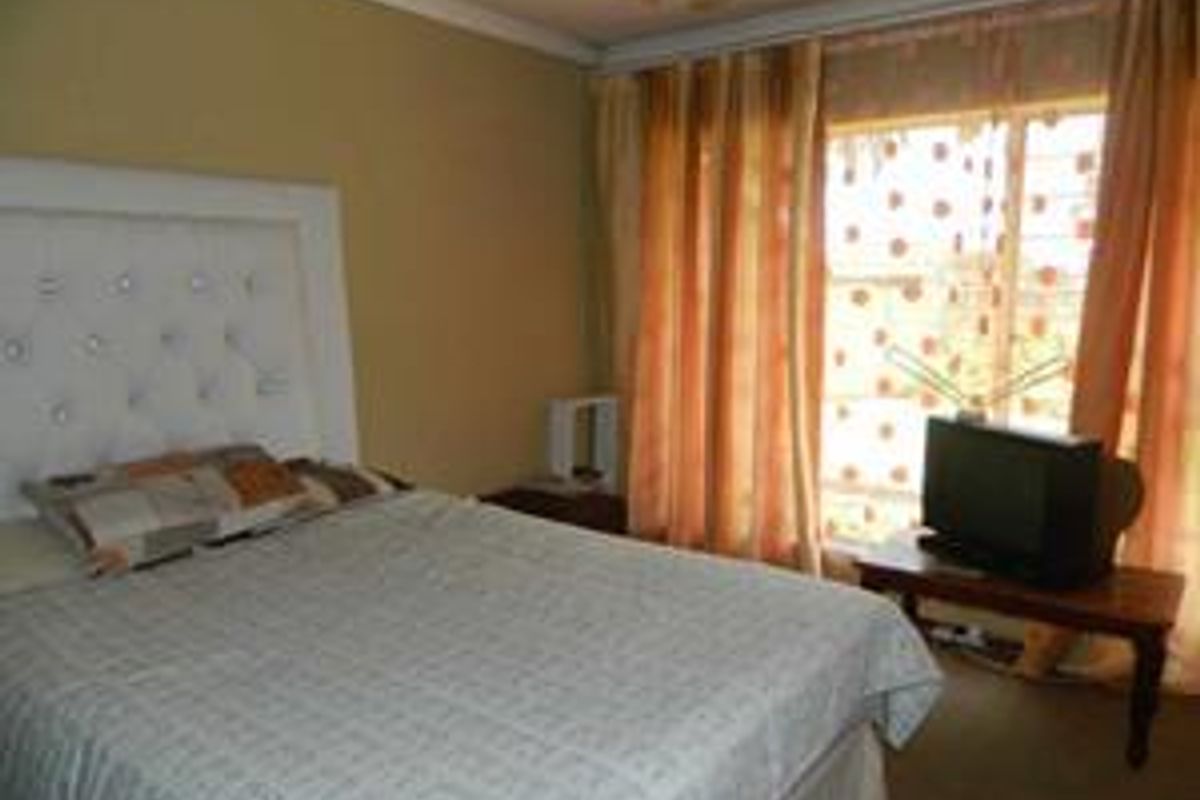 A standard bedroom featuring neutral wall paint, coving, and a large window with security bars, providing natural light.