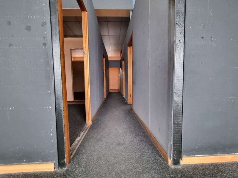 A long, empty commercial hallway featuring dark painted walls, timber door frames, and carpeted flooring, leading to multiple office or utility rooms.