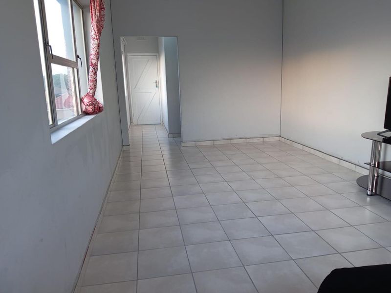 An empty living area featuring neutral tiled flooring and access to an internal hallway, providing a blank canvas for interior design.