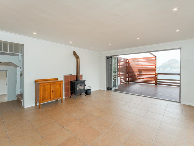 Spacious living area featuring tiled floors, a freestanding fireplace, and large stacking doors opening onto a timber deck with scenic mountain and water views.