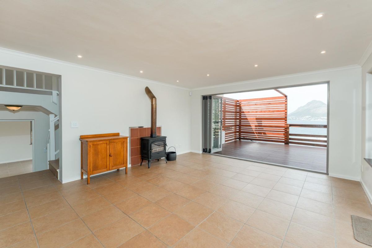 Spacious living area featuring tiled floors, a freestanding fireplace, and large stacking doors opening onto a timber deck with scenic mountain and water views.