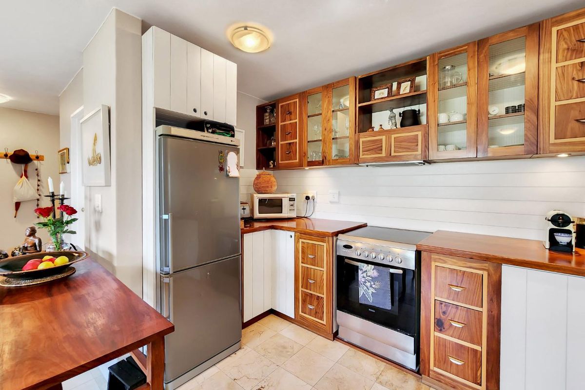 A functional kitchen featuring a mix of white and natural wood cabinetry, stone tile flooring, and integrated appliances with wooden countertops.