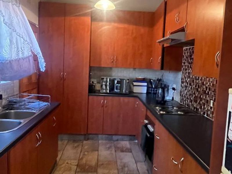A functional kitchen featuring warm-toned wooden cabinetry, dark countertops, a built-in hob with extractor fan, and distinctive exposed timber ceiling beams.