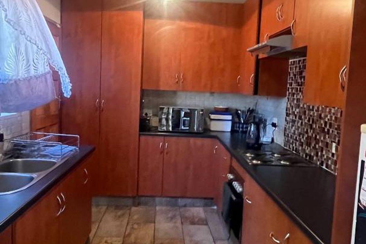 A functional kitchen featuring warm-toned wooden cabinetry, dark countertops, a built-in hob with extractor fan, and distinctive exposed timber ceiling beams.