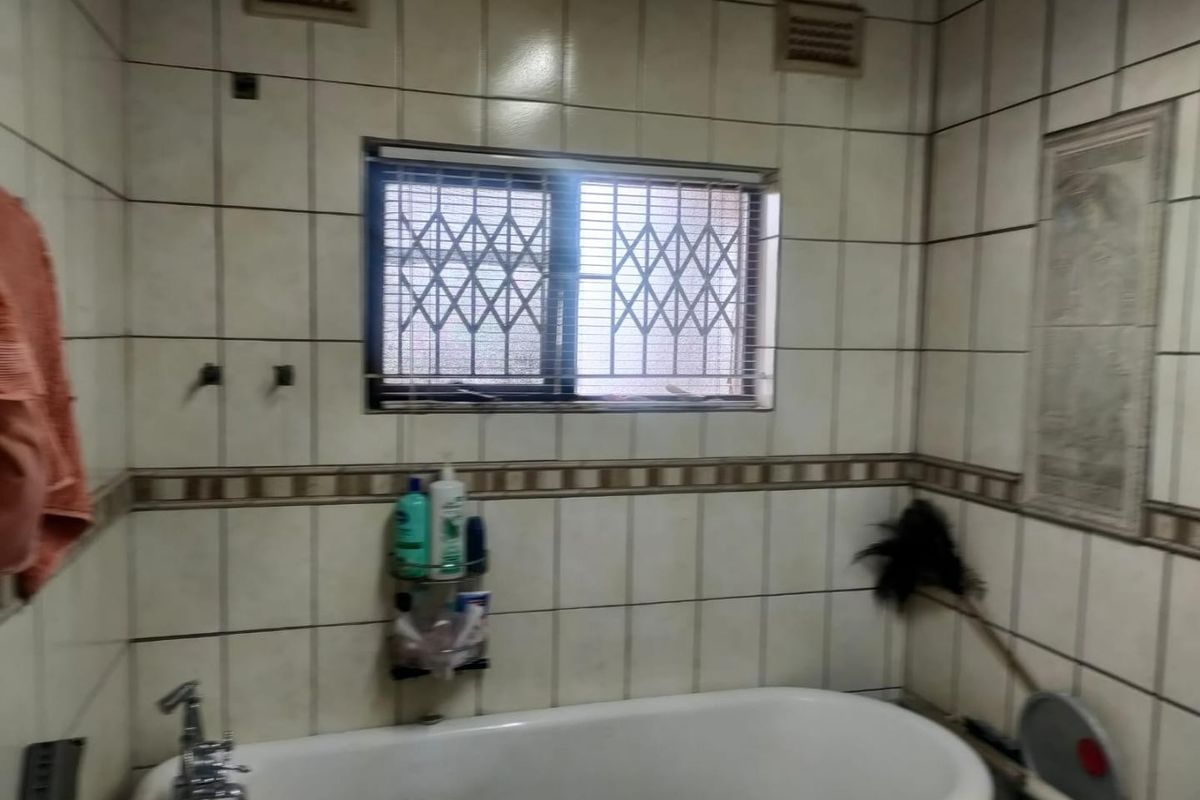 A dated bathroom featuring a standard bathtub, tiled walls with decorative border, and a window fitted with a security gate.