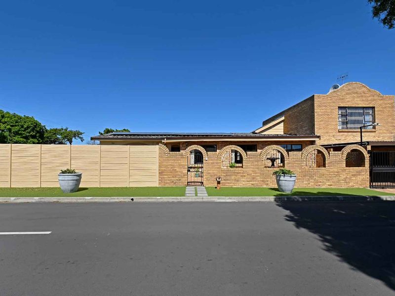 Front street-facing view of the property featuring a brick boundary wall, arched entrance gate, and solar panels installed on the roof.