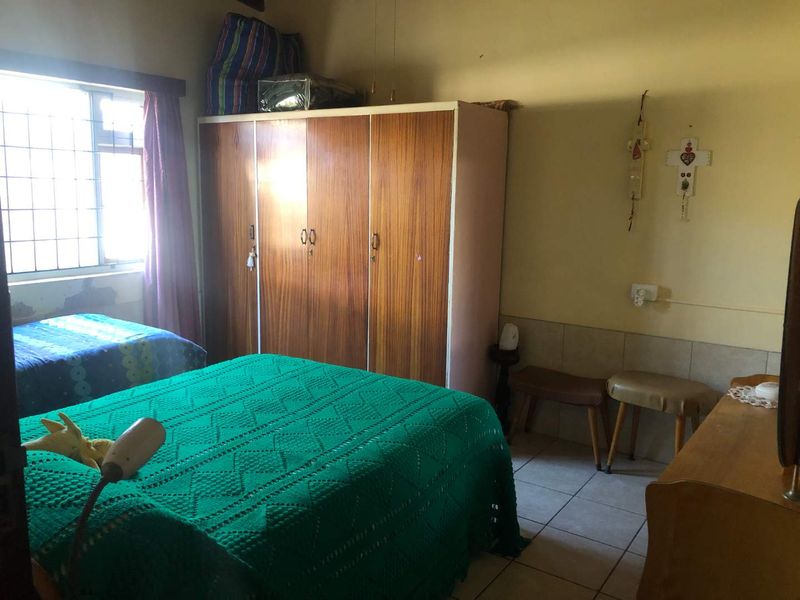 A bedroom featuring tiled flooring, a built-in wooden wardrobe, and security bars on the window, showing signs of wear and paint damage.